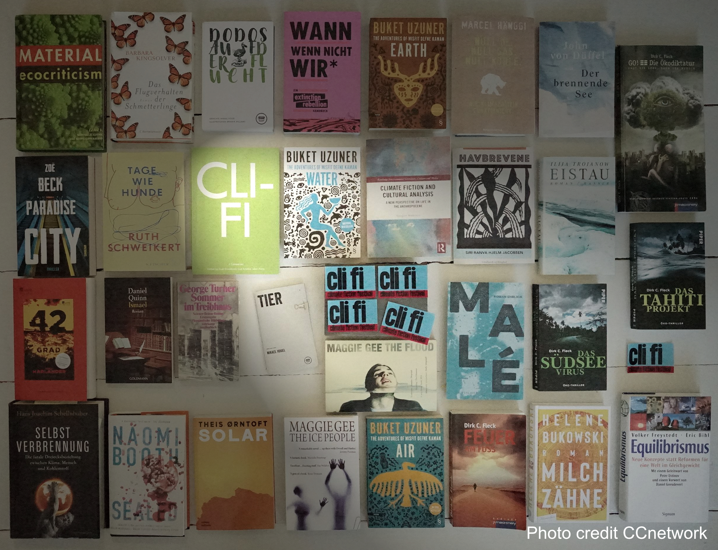 30 Bücher aus dem großen Feld der Klimaliteratur liegen nebeneinander auf dem Boden. In der Mitte beleuchtet ein Spottlicht 
            ein Cover mit der Abkürzung cli fi
